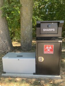 gray metal lock box next to a black metal sharps disposal container with red and white biohazard sign